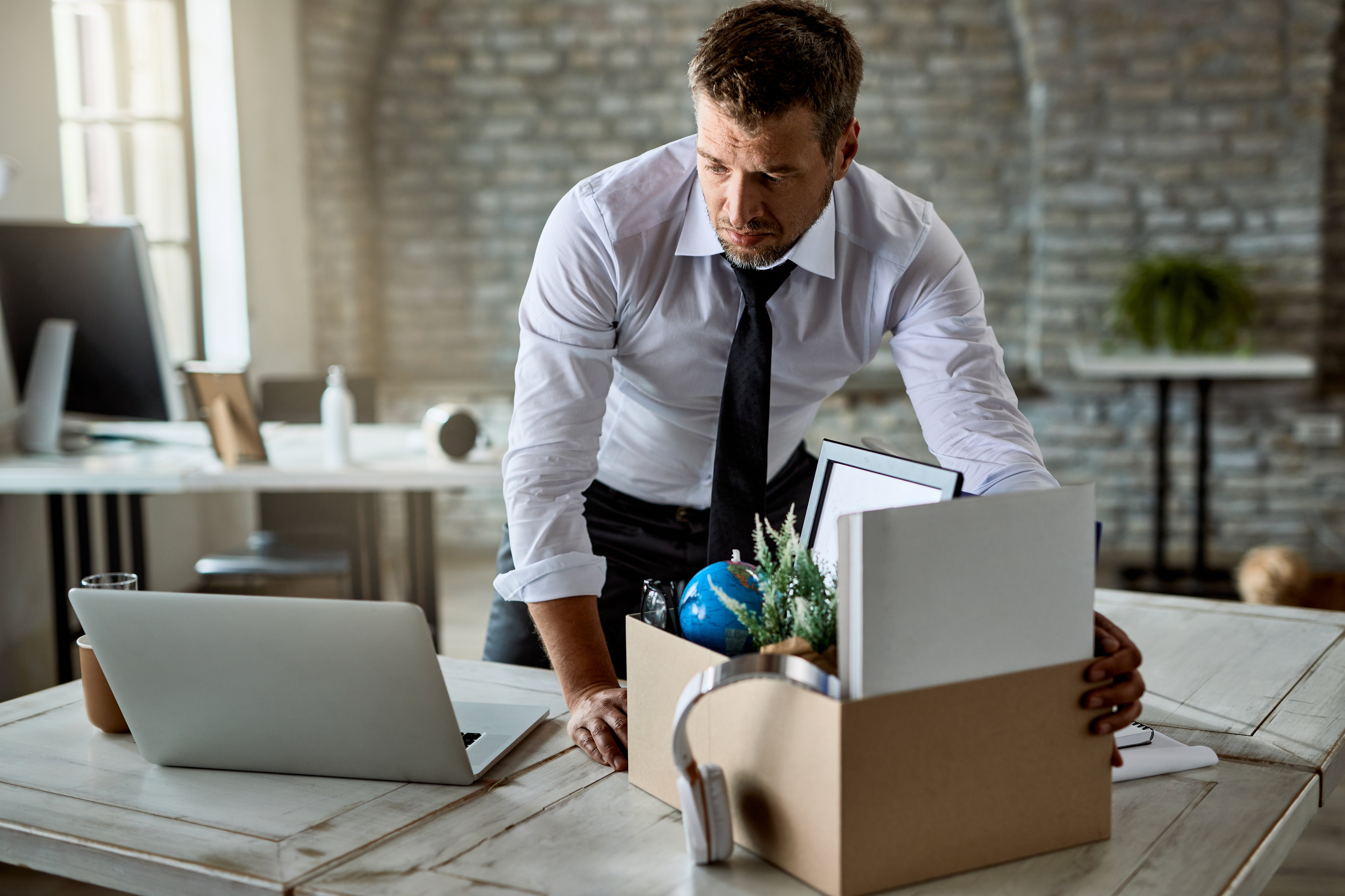 sad entrepreneur packing his belongings cardboard box while leaving office after losing his job