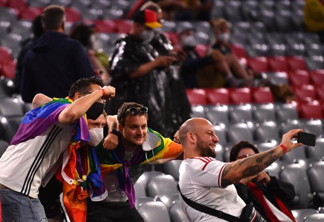 Aficionados de Hungría y de Alemania, fotografiándose con un seguidor que porta una bandera LGTBI