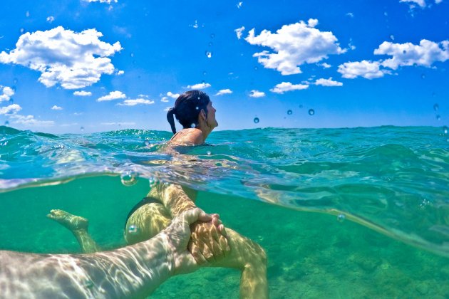 Un hombre y una mujer agarrados de la mano en el mar : Unplash