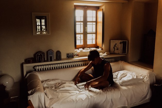 Un hombre lee en su cama a plena luz del día / Unsplash