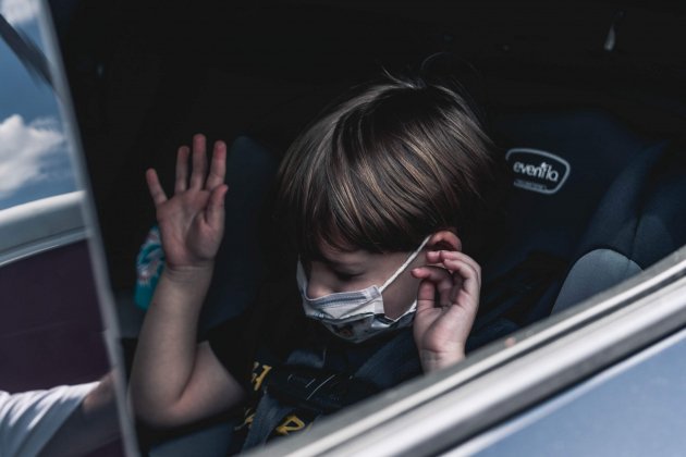 Un niño con mascarilla sentado en su silla del coche / Unsplash