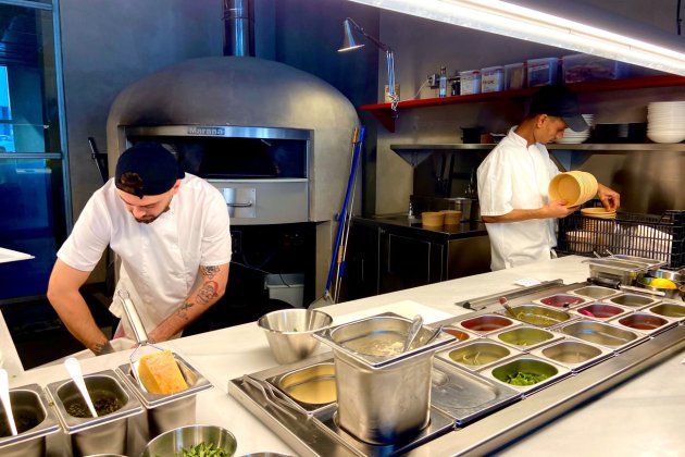 El dúo en la cocina prepara las pizzas desde cero con los condimentos frescos en frente / Foto: Oriol Foix