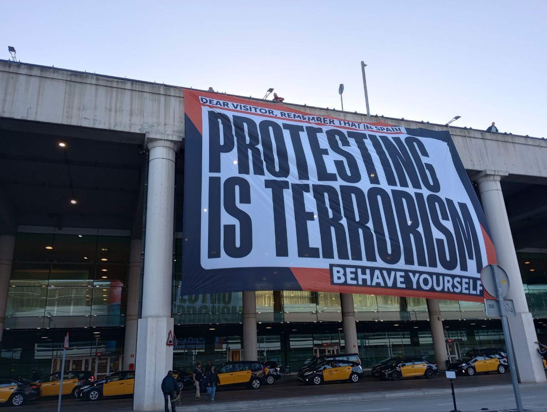 Òmnium unfurls Barcelona airport banner, warning visitors: "In Spain, protesting is terrorism"