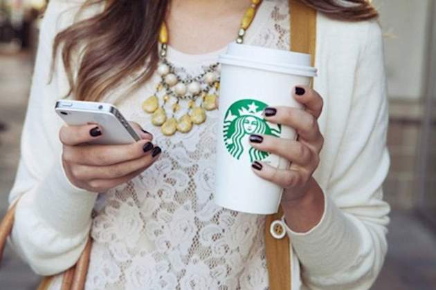 Joven usando un iPhone mientras sujeta un café de Starbucks