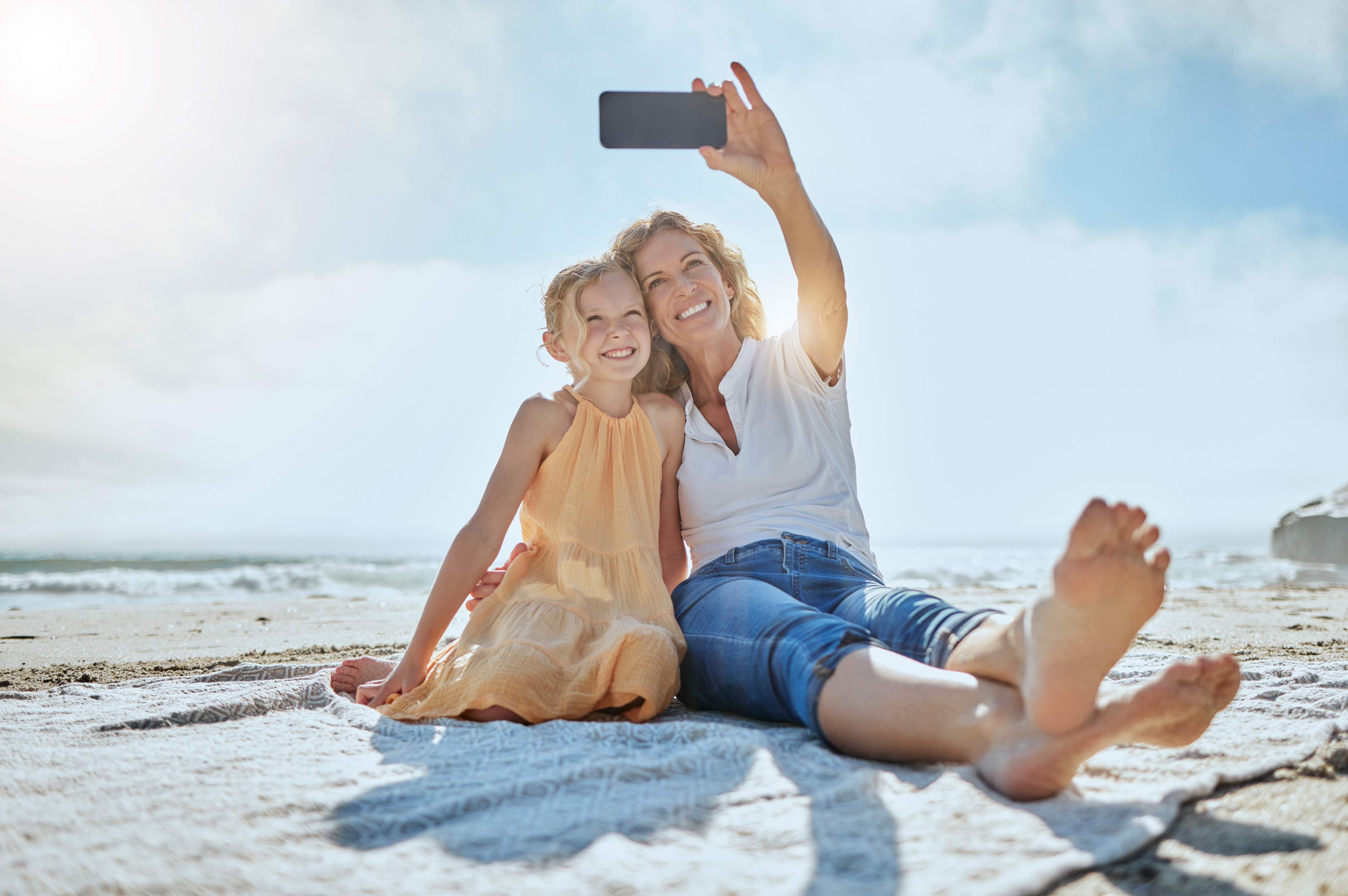 carefree mother daughter taking selfie while sitting beach happy little girl grandmother smiling while taking picture cellphone while holiday mom daughter bonding