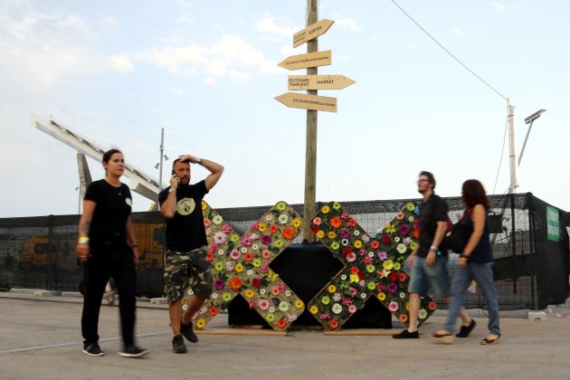 Assistents al Festival Cruïlla passen davant d'un panell del festival. Pau Cortina.